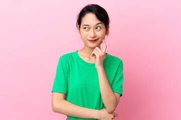 Young Vietnamese woman isolated on pink background having doubts and thinking