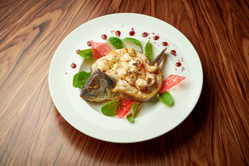 Baked dorado fish with cauliflower and cheese in a white plate on a wooden background