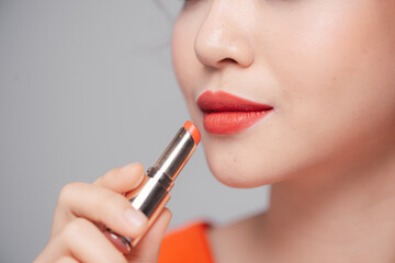 Beautiful young woman putting lipstick on lips