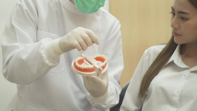 A caucasian dentist man, people showing how to use dental floss with typodont teeth model to Asian patient at hospital clinic. Cleaning. Doctor. Dentistry, medical and health.