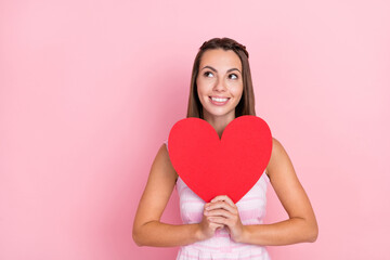 Photo of dreamy happy positive young woman look empty space hold heart shape isolated on pink color background