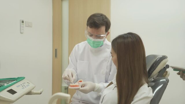 A caucasian dentist man, people showing how to use dental floss with typodont teeth model to Asian patient at hospital clinic. Cleaning. Doctor. Dentistry, medical and health.