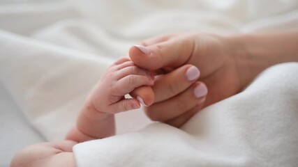 Mother holding tiny hand of newborn baby and petting it. Parent of adorable infant cares about his child at home with tenderness - Powered by Adobe