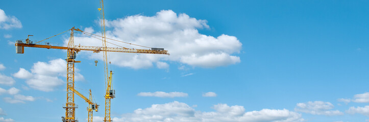 Panorama with many tower cranes in clear blue sky with clouds