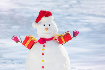 Decorated Snowman in red hat with a gift boxes at winter day.