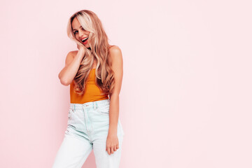 Naklejka premium Portrait of young beautiful smiling female in trendy summer clothes. Sexy carefree blond woman posing near pink wall in studio. Positive model having fun indoors. Cheerful and happy