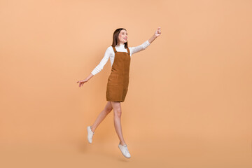Fototapeta na wymiar Full body profile portrait of active cheerful girl raise arm look empty space isolated on beige color background