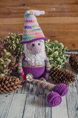 Crochet purple dwarf with a bell on a wooden background with cones and dried flowers.