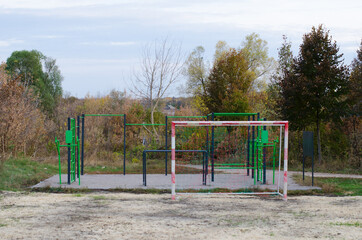Fototapeta na wymiar An outdoor sports ground with green and black metal equipment and part of soccer field with football goal in the park with autumn trees. 