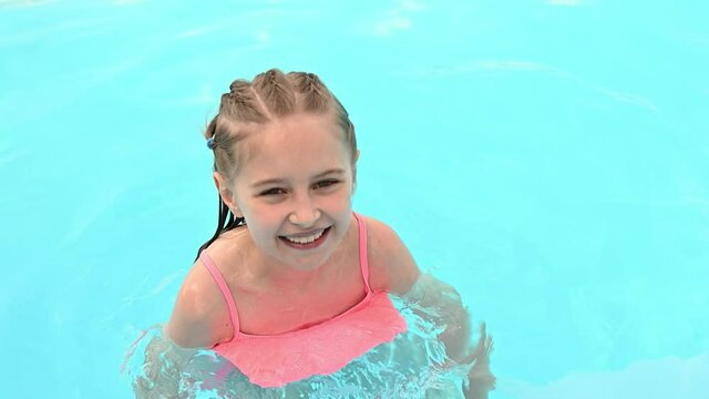 Preteen girl swimming in pool and smiling in sunny summer day outside. Female kid jumping in the water at resort on vacation