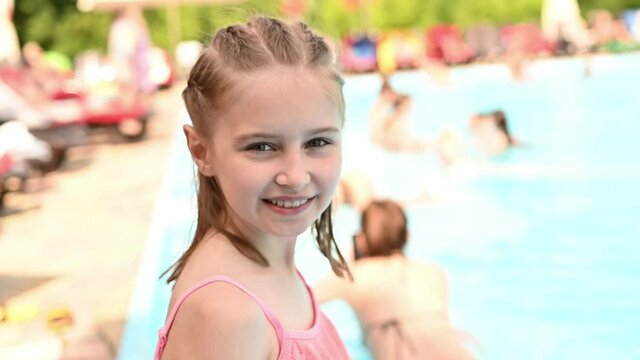 Preteen girl in swimming pool posing and smiling. Pretty female kid in the water at resort on vacation in summer time