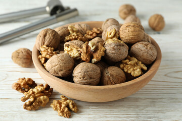 Nutcracker and bowl of walnuts on white wooden background
