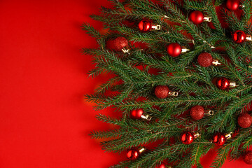 Christmas tree made of green coniferous branches on a red background. Christmas background with place for text. Christmas holiday concept. Ball toys. Copy space.