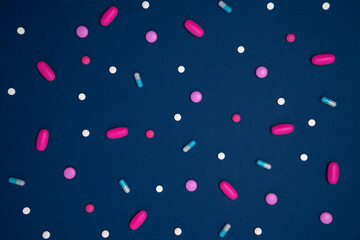 Blue background with many drugs in capsules and tablets of different colors scattered on the surface