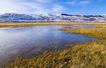 Naklejka premium Winter landscape in Patagonia: frozen lake on the pampas with snow covered hills in the background