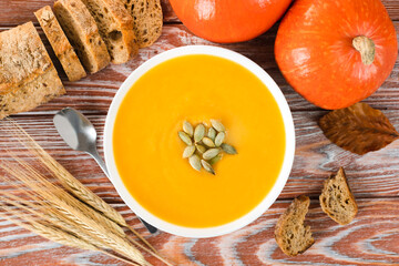 Pumpkin cream soup with rye bread and pumpkins on a wooden background. Seasonal vegetables menu....
