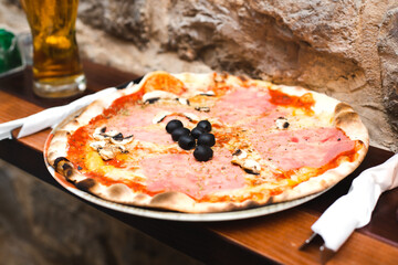 Delicious pizza with prosciutto, mushrooms, tomato paste and olives in a outdoor cafe. Selective focus. Close-up.