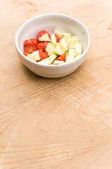 fresh zucchini and datterini tomatoes chunks in a white bowl on a rustic wooden background