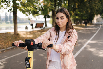 Young woman riding an electric scooter on a meeting. Ecological transportation concept. Attractive female outdoors with e-scooter