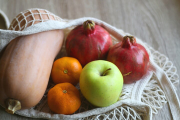 Crochet bag filled with butternut squash, pomegranates, apples and tangeriens. Selective focus.