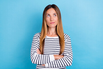 Fototapeta premium Photo of charming unsure young woman dressed striped pullover looking empty space arms crossed isolated blue color background