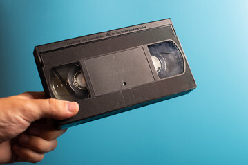 Hand holds retro HVS video cassette on a blue background. Retro wave. 80s 90s