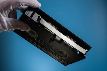 Hand holds retro HVS video cassette on a blue background. Retro wave. 80s 90s. Open film.