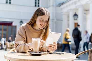 A woman uses a tablet. Sitting in a summer cafe on the street. Online training. A teenager communicates with friends on a social network. The blogger writes a message to the mail.