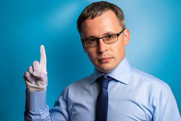 A serious man in a blue shirt and tie shows his index finger raised up with a hand in a white glove. Confident specialist on a blue background.