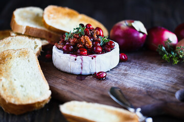 Baked Camembert Brie cheese with a cranberry, honey, balsamic vinegar and nut relish and garnished with thyme. Served with toasted bread slices. Selective focus with blurred background and foreground.
