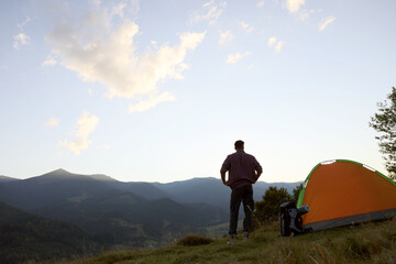 Tourist with backpack and sleeping pad near camping tent in mountains