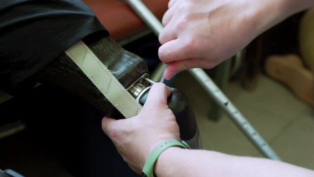 Close view: an engineer's hands checking the artificial bionic leg prothesis device unscrewing its parts. Maintenance of modern bionic legs prothesis for man living with disability with amputated legs