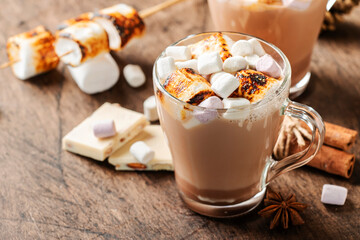 Hot chocolate drink with fried marshmallow in glass cups and winter decoration on wooden table. Concept of cosy Christmas and New Year holidays