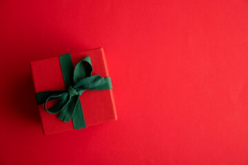 Festive christmas gift box present tied with a rustic ribbon and bow on a red background. Overhead view