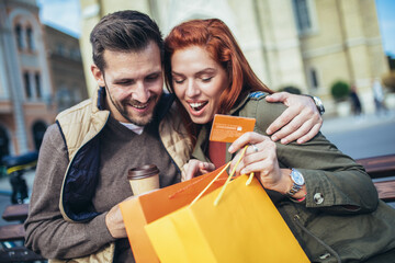 Portrait of happy couple with shopping bags after shopping in city smiling and holding credit card