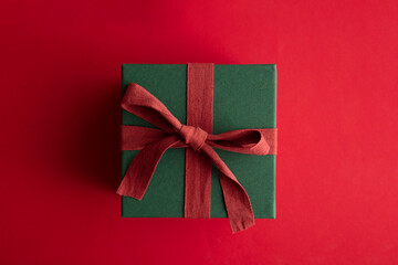 Festive christmas gift box present tied with a rustic ribbon and bow on a red background. Overhead view
