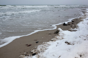 winter landscape sandy beach, coastline with pebbles, snow and sea waves