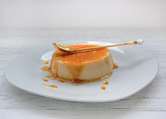 sweet flan egg dessert with caramel crust on a white plate with a spoon, top view