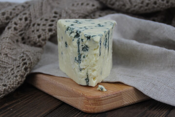 piece of delicious cheese with blue mold on a wooden cutting board. rustic background - knitted and linen textile