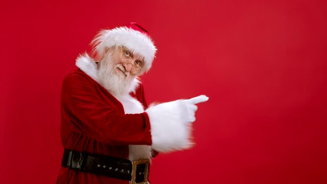 Funny Santa Claus Pointing at Copy Space, Showing Workspace Mockup for Advertisement, Empty Place for Text or Image, Promotional Content. Studio Shot on Red Background. Sale, Discount, Black Friday.