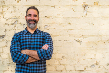 Portrait of modern businessman with beard standing in front of brick wall outdoor.	