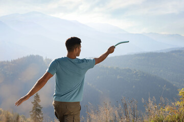 Man throwing boomerang in mountains on sunny day, back view - obrazy, fototapety, plakaty
