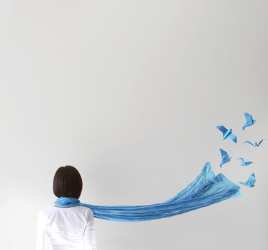Rear view of woman's blue scarf flying away as conceptual origami birds