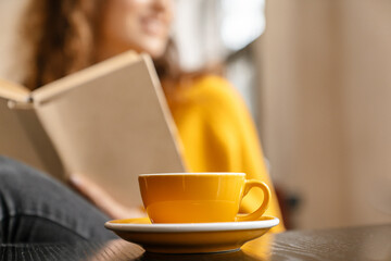 Young white woman reading book while drinking coffee in cafe