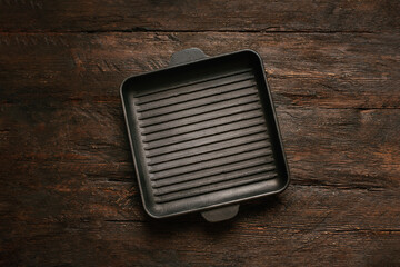 New empty cast-iron grill pan with two handles on wooden background.