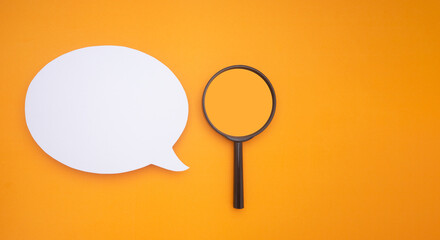 Top view of a blank white speech bubble and a magnifying glass isolated on a yellow background....