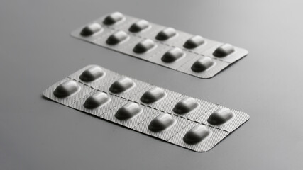 Two gray metallized blisters with medical pills or capsules on a gray background. Duotone. Aspect ratio 16 to 9