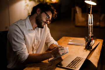 White man in eyeglasses talking on cellphone while working with laptop