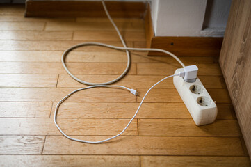 Phone charger plugged in an old power extension lead. Vintage looking room environment with wooden floor.