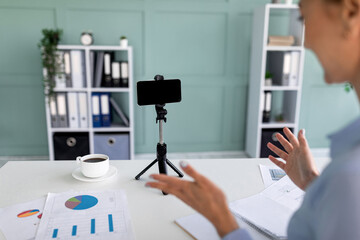 Female business blogger recording video on smartphone and telling about successful freelance career